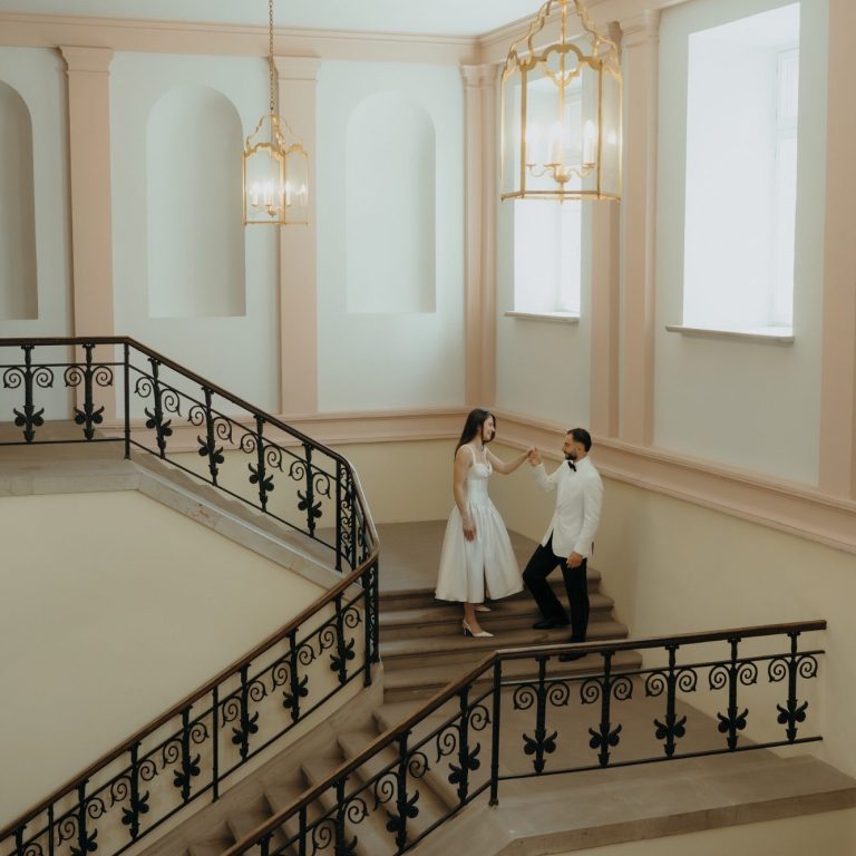 Hochzeitsreportage Ein Paar steht an einer Treppe in einem eleganten Innenraum. Helle Farben und Kunstlicht.