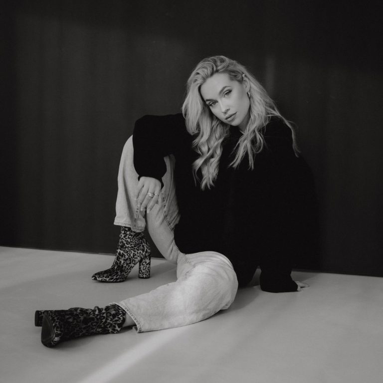 Portrait Shooting Eine blonde Frau sitzt lässig auf dem Boden in einem modischen Outfit.